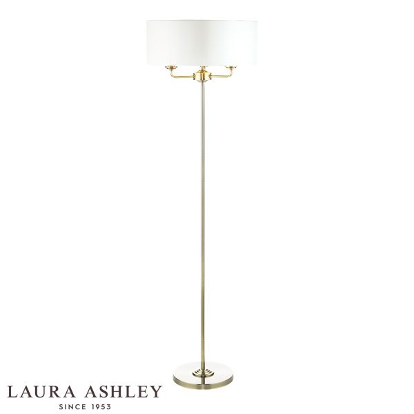Sorrento 3 light floor lamp in antique brass finish with ivory faux silk shade, on white background, lit.