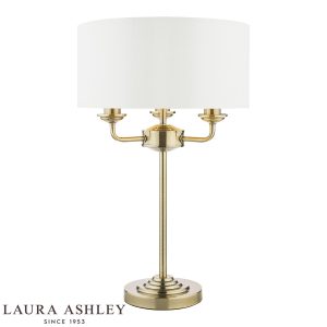 Sorrento 3 light table lamp in antique brass finish with ivory faux silk shade on white background, lit.