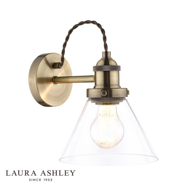 Laura Ashley Isaac single wall light in antique brass finish with clear glass shade on white background.