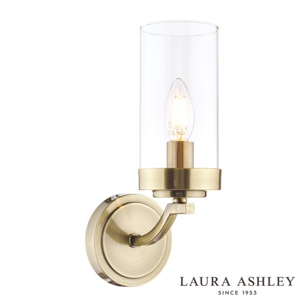 The Laura Ashley Joseph single wall light in antique brass with glass shade, on white background, lit.