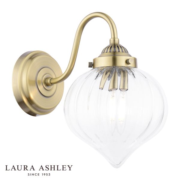 Whitham single wall light in antique brass finish with clear ribbed glass teardrop shade on white background, lit.
