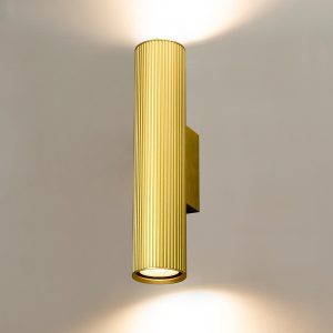 Franklite Scout modern up and down wall light in aged brass, on cream wall, lit.