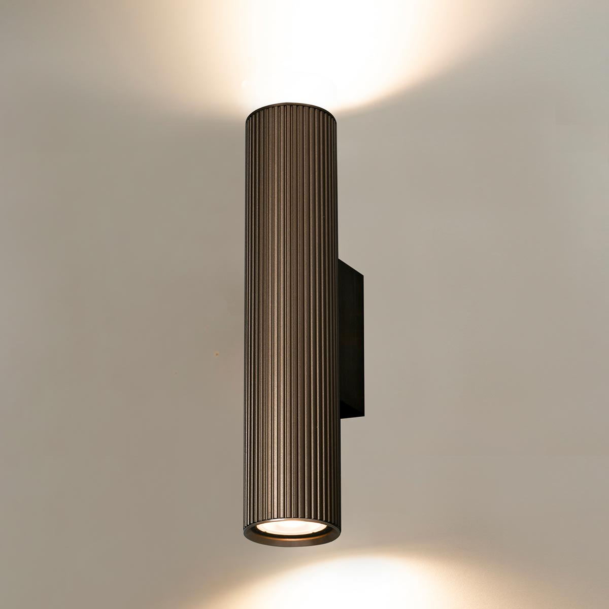 Franklite Scout modern up and down wall light in bronze, on cream wall, lit.
