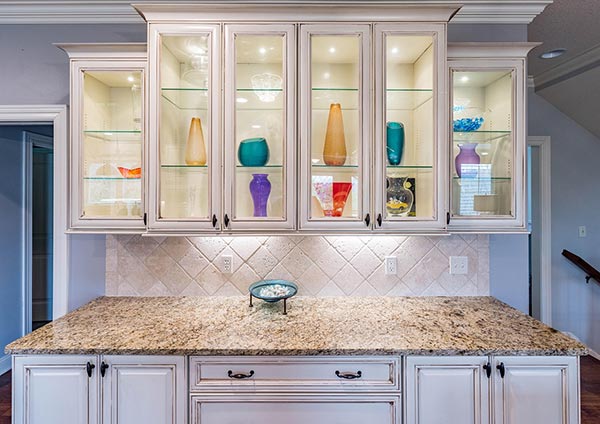 Worktop with glass cabinets above in kitchen, with downlights fitted inside the cupboards and under cupboard lighting.
