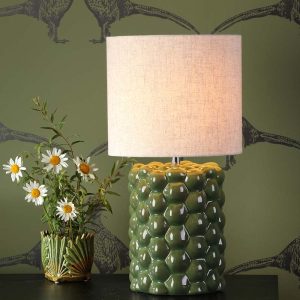 Jayden ceramic table lamp with green reactive glaze and linen shade, on sideboard in living room setting lit