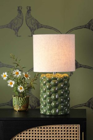 Jayden ceramic table lamp with green reactive glaze and linen shade, on sideboard in living room setting lit